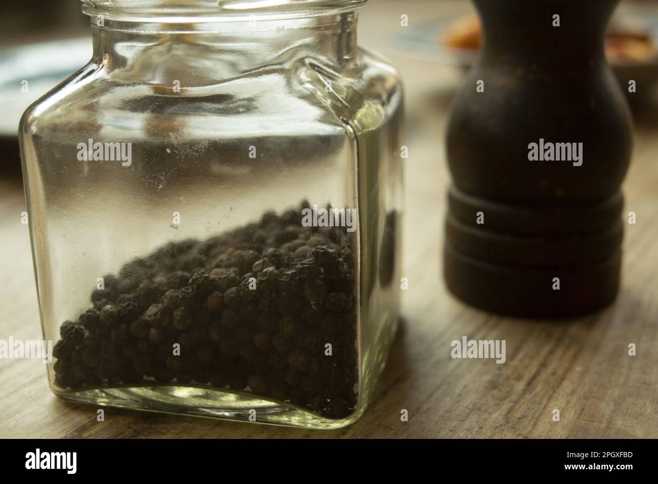 grani di pepe nero in un vaso di vetro con un tritacarne sullo sfondo Foto Stock