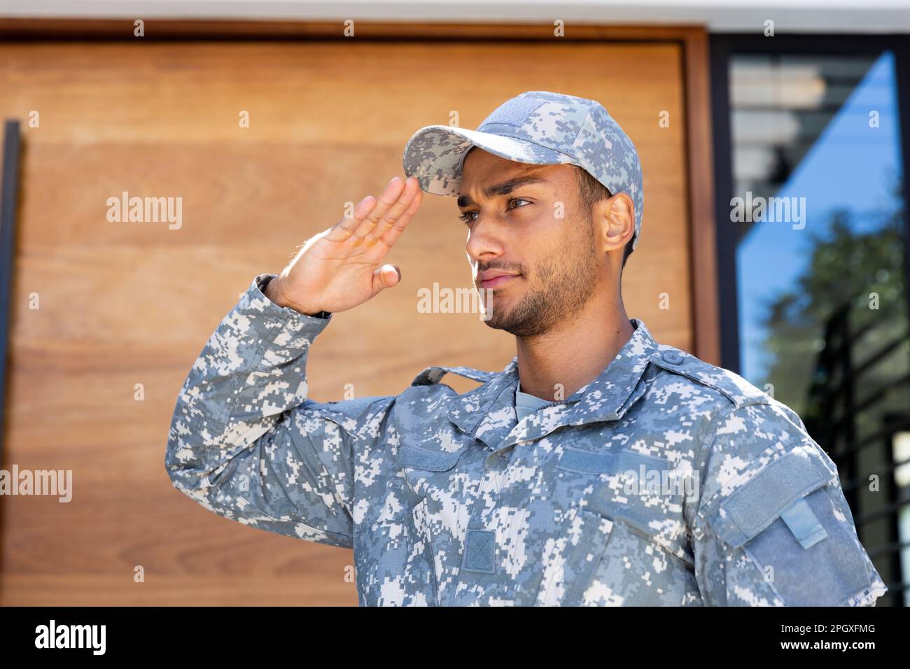 Soldato biraciale maschio che indossa uniforme e cappuccio, saluta fuori casa Foto Stock