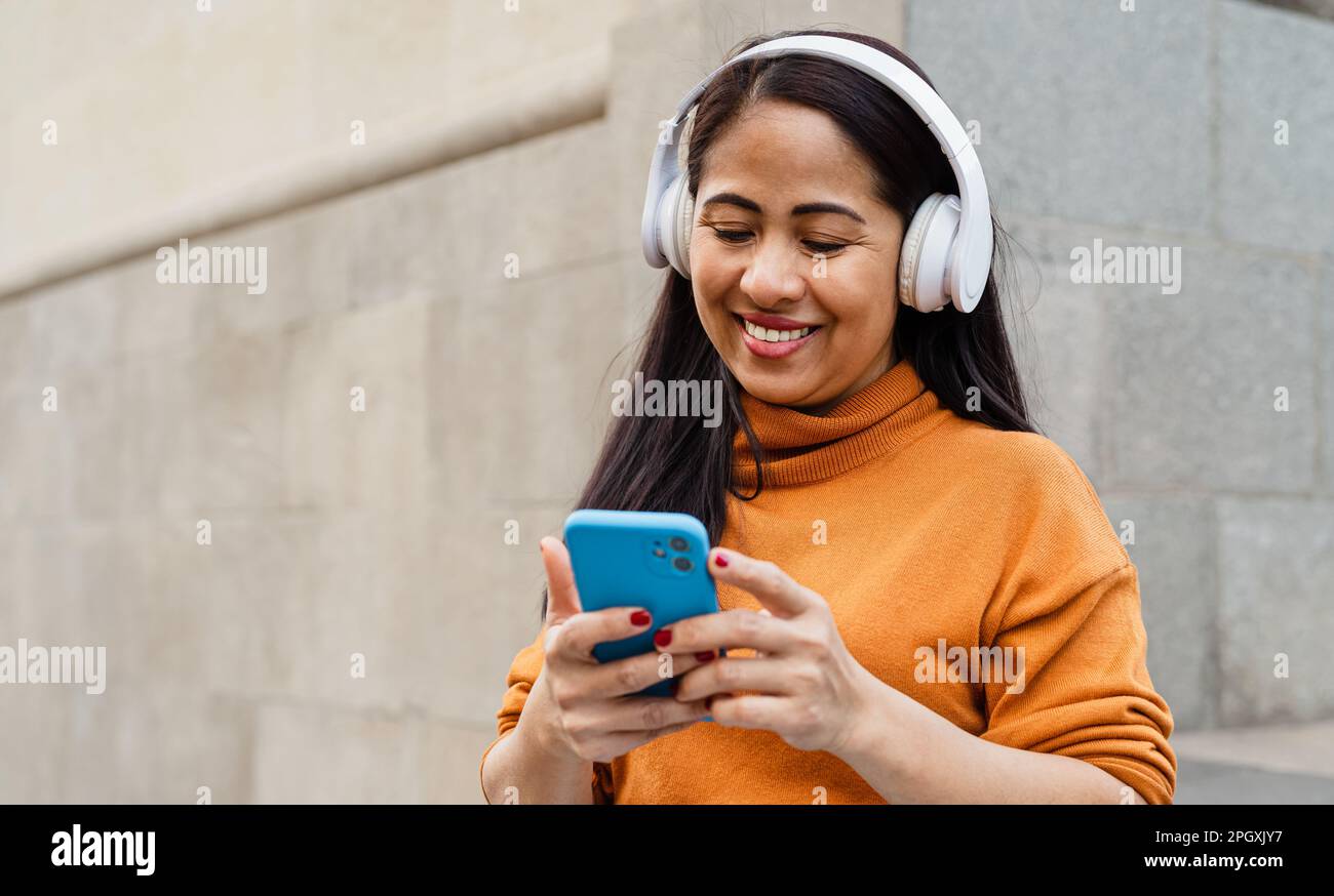 Felice donna del sud-est asiatico che ascolta musica con smartphone e cuffie mobili nel centro della città Foto Stock