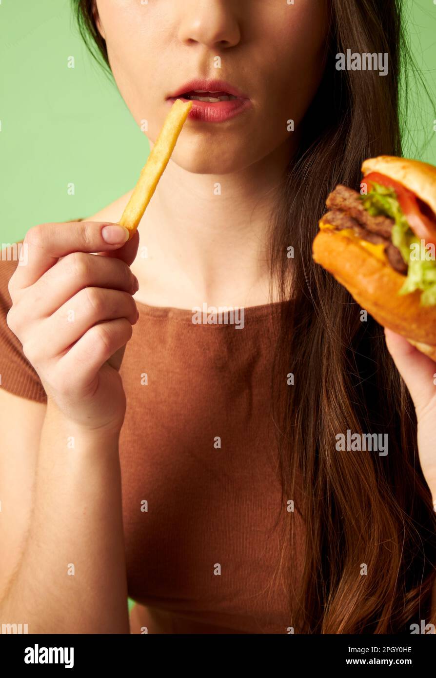 Ritratto di donna che tiene hamburger cheeseburger mentre mangiare frittura francese Foto Stock