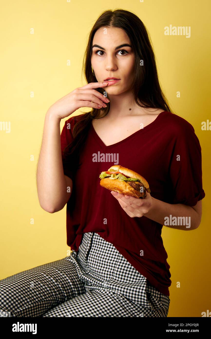 Donna leccando le dita dopo aver mangiato hamburger in mano Foto Stock