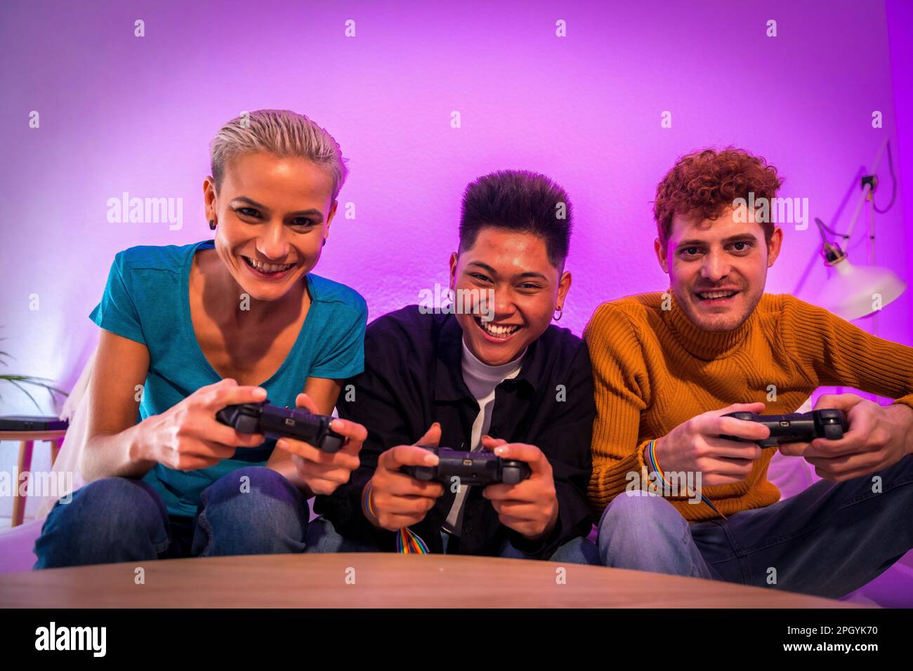 Gruppo di giovani amici che giocano insieme sul divano di casa, sfidando guardando la fotocamera Foto Stock