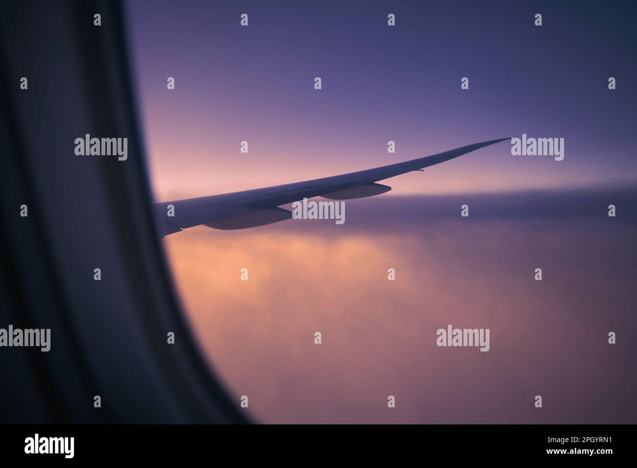 Vista dalla finestra dell'aereo durante il volo sopra le nuvole all'alba. Focalizzazione selettiva sull'ala dell'aeromobile. Foto Stock