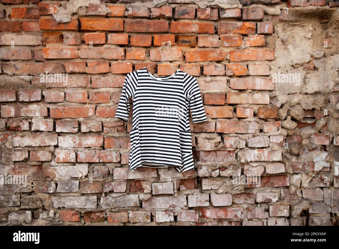 blusa donna a righe bianche e nere appesa su una vecchia parete di mattoni all'aperto al sole Foto Stock