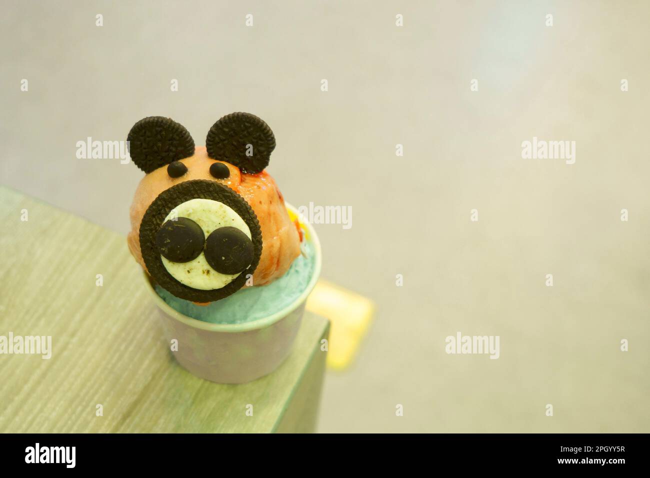 Una tazza di gelato con la guarnizione di biscotto simile al topo servita sul tavolo di legno con fondo sfocato. Foto Stock