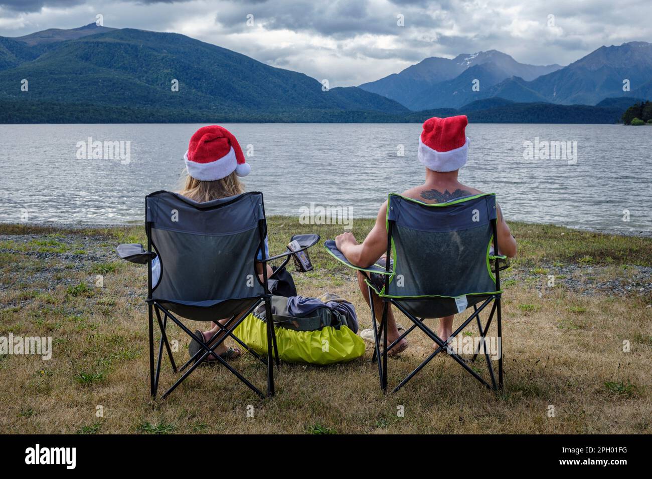 Una coppia che indossa cappelli di Natale guarda il sole tramontare la vigilia di Natale al lago te Anau, South Island, Nuova Zelanda Foto Stock