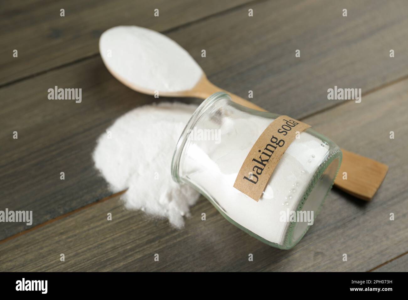 Vaso rovesciato e cucchiaio con bicarbonato su tavolo di legno, primo piano Foto Stock