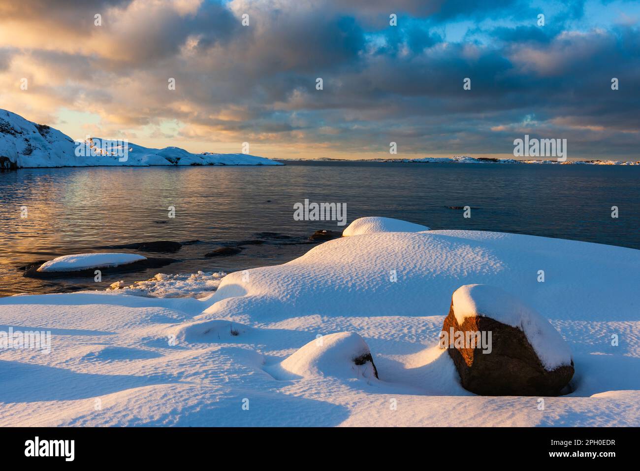Una pittoresca scena invernale della costa svedese, che riflette un bellissimo tramonto nelle sue acque ghiacciate. La terra coperta di neve e il mare si fondono insieme Foto Stock