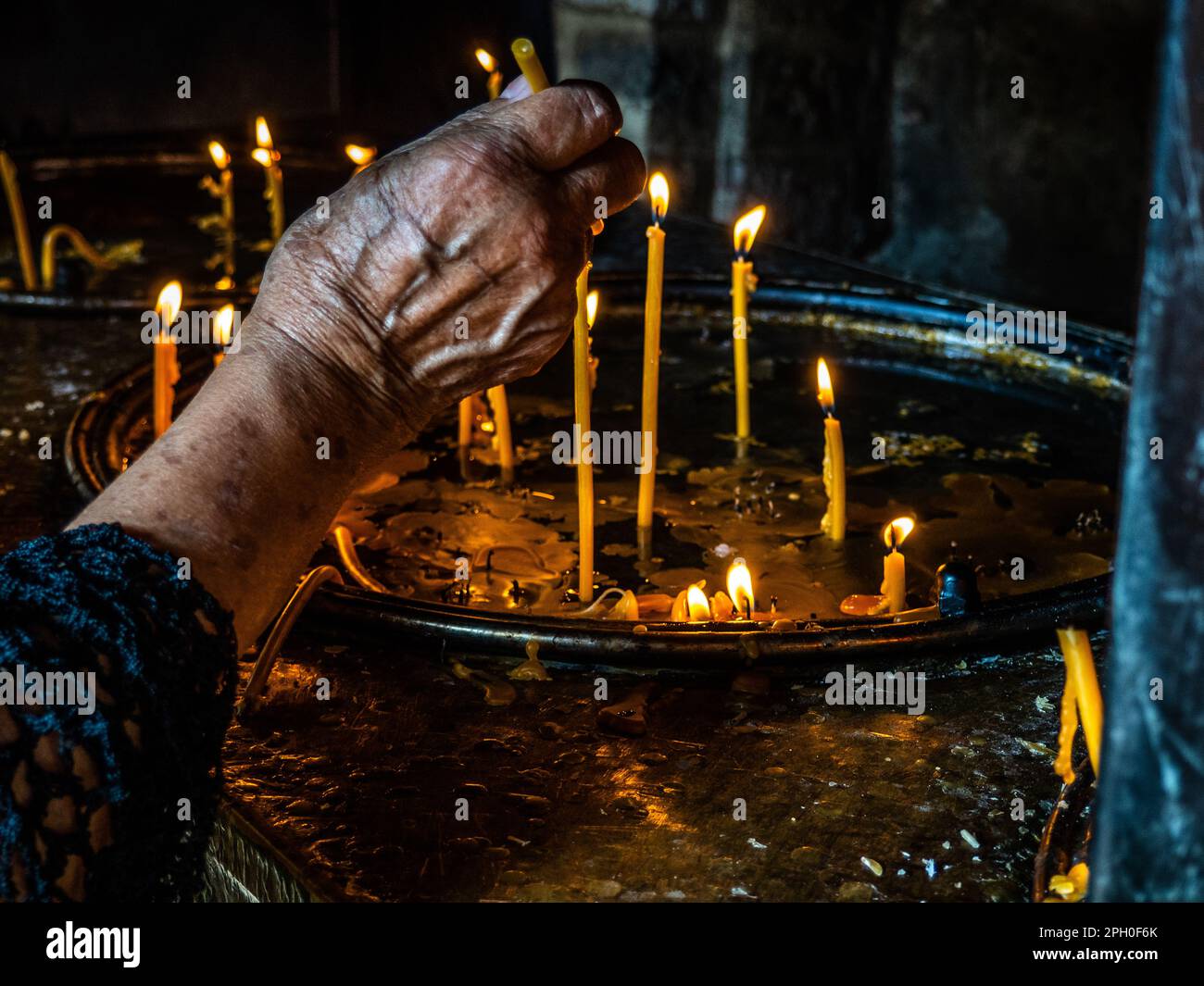 la mano della donna anziana che illumina una candela in chiesa Foto Stock