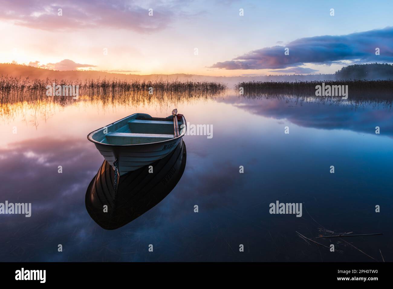 Un'alba tranquilla con una barca a remi che si riflette sulla superficie serena dei laghi, circondata dalla bellezza della natura e da un cielo rosa. Foto Stock