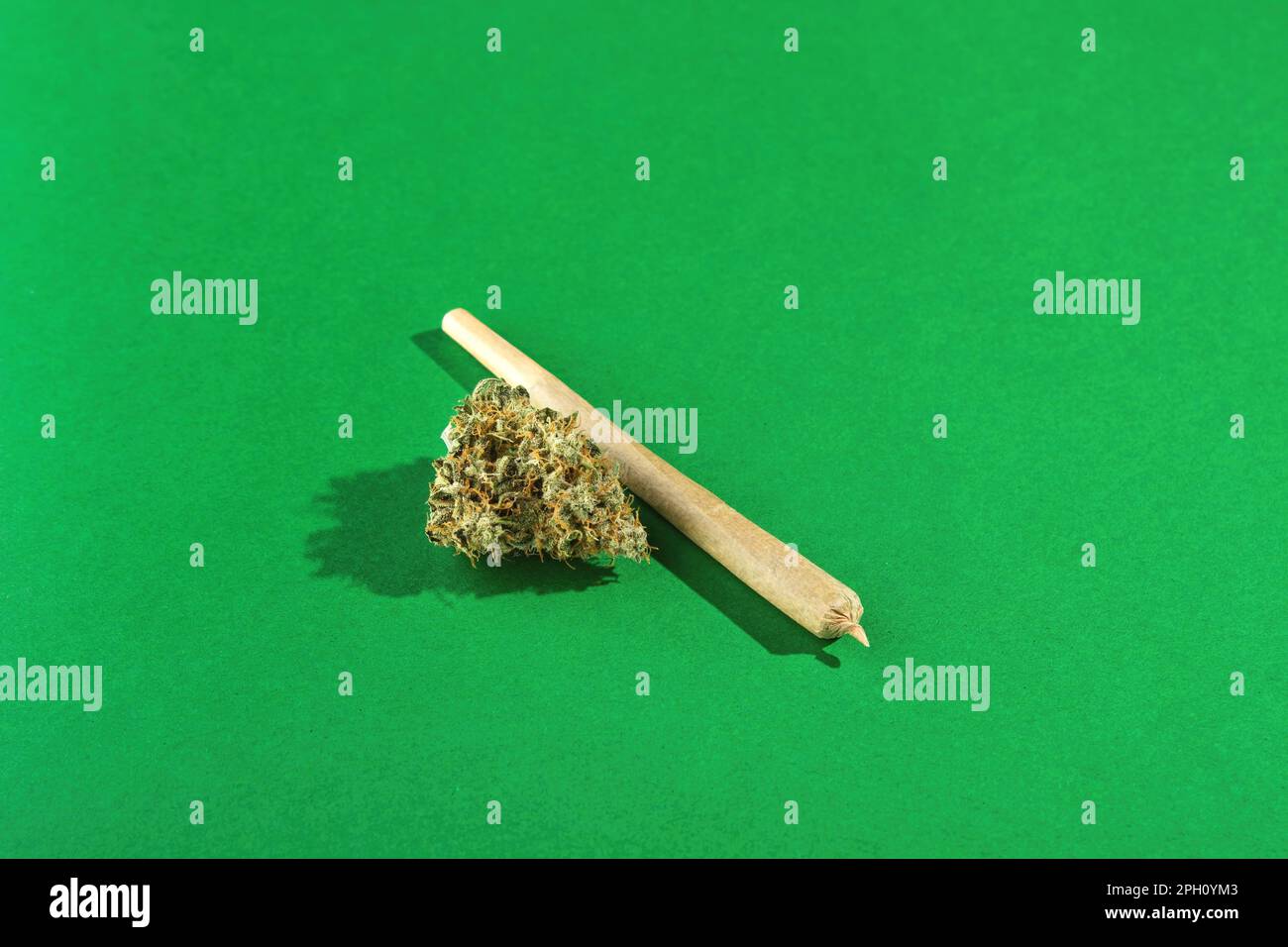 Un giunto di dimensioni reali si trova accanto a germogli di marijuana asciutti su uno sfondo verde. Molto spazio vuoto Foto Stock