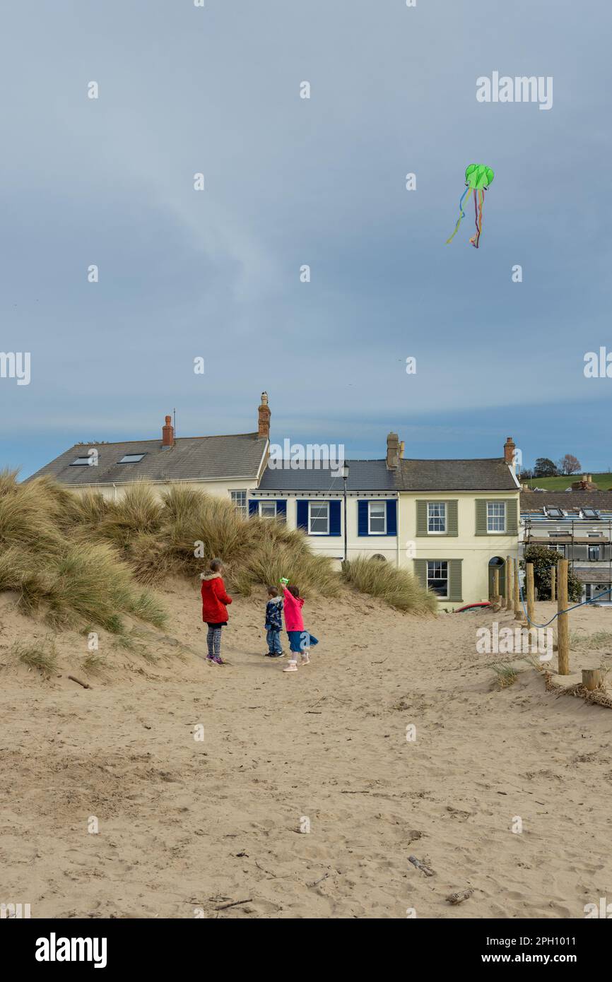 Una famiglia che indossa giacche rosse cammina tra le dune di sabbia del Devon mentre vola con un aquilone verde Foto Stock