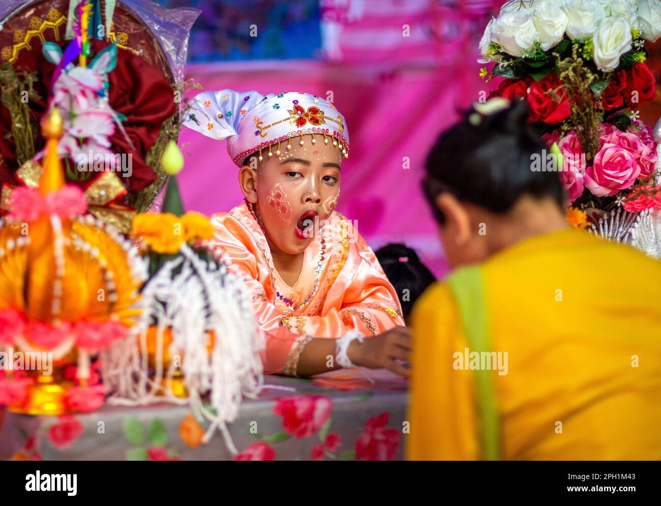 Un giovane ragazzo di etnia Shan vestito di costume colorato si sbadigia durante il festival POY Sang Long, una celebrazione di rito dell'ordinazione dei novizi buddisti al tempio di Wat Ku Tao. POY Sang Long è una cerimonia di ordinazione dei novizi buddisti tra il popolo Shan chiamato anche tribale Tai Yai in Myanmar e nella parte settentrionale della Thailandia, ma a differenza di qualsiasi altra cerimonia del suo tipo nel paese. I ragazzi di età compresa tra i sette e i 14 anni, noti come "figli di Cristallo", saranno ordinati novizi per imparare le dottrine buddiste per guadagnare meriti ai loro genitori e alle loro famiglie. Foto Stock