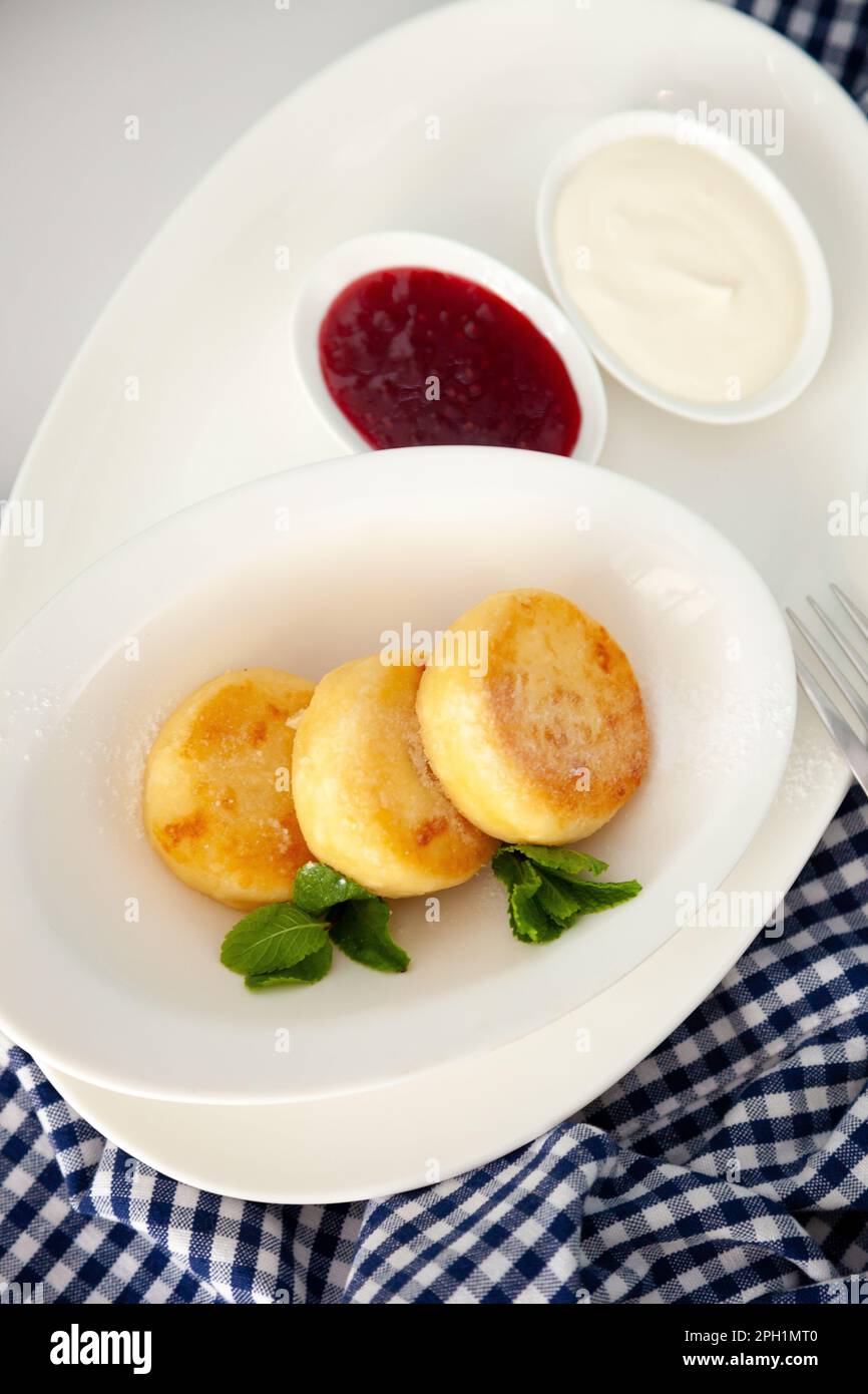 Frittelle di formaggio ricotta rotonda in un piatto bianco su sfondo blu. Cibo prima colazione. Cibo sano. Salsa di panna acida e menta. Primo piano vista dall'alto. Pasto dessert. Frittelle di ricotta al formaggio ricotta. Foto Stock