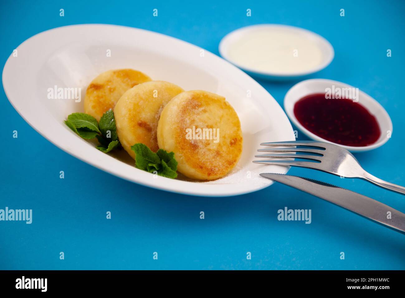 Frittelle di formaggio ricotta rotonda in un piatto bianco su sfondo blu. Cibo prima colazione. Cibo sano. Salsa di panna acida e menta. Primo piano vista dall'alto. Pasto dessert. Frittelle di ricotta al formaggio ricotta. Foto Stock