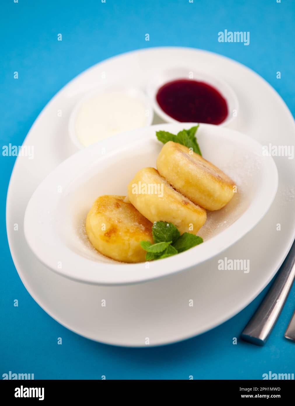 Frittelle di formaggio ricotta rotonda in un piatto bianco su sfondo blu. Cibo prima colazione. Cibo sano. Salsa di panna acida e menta. Primo piano vista dall'alto. Pasto dessert. Frittelle di ricotta al formaggio ricotta. Foto Stock