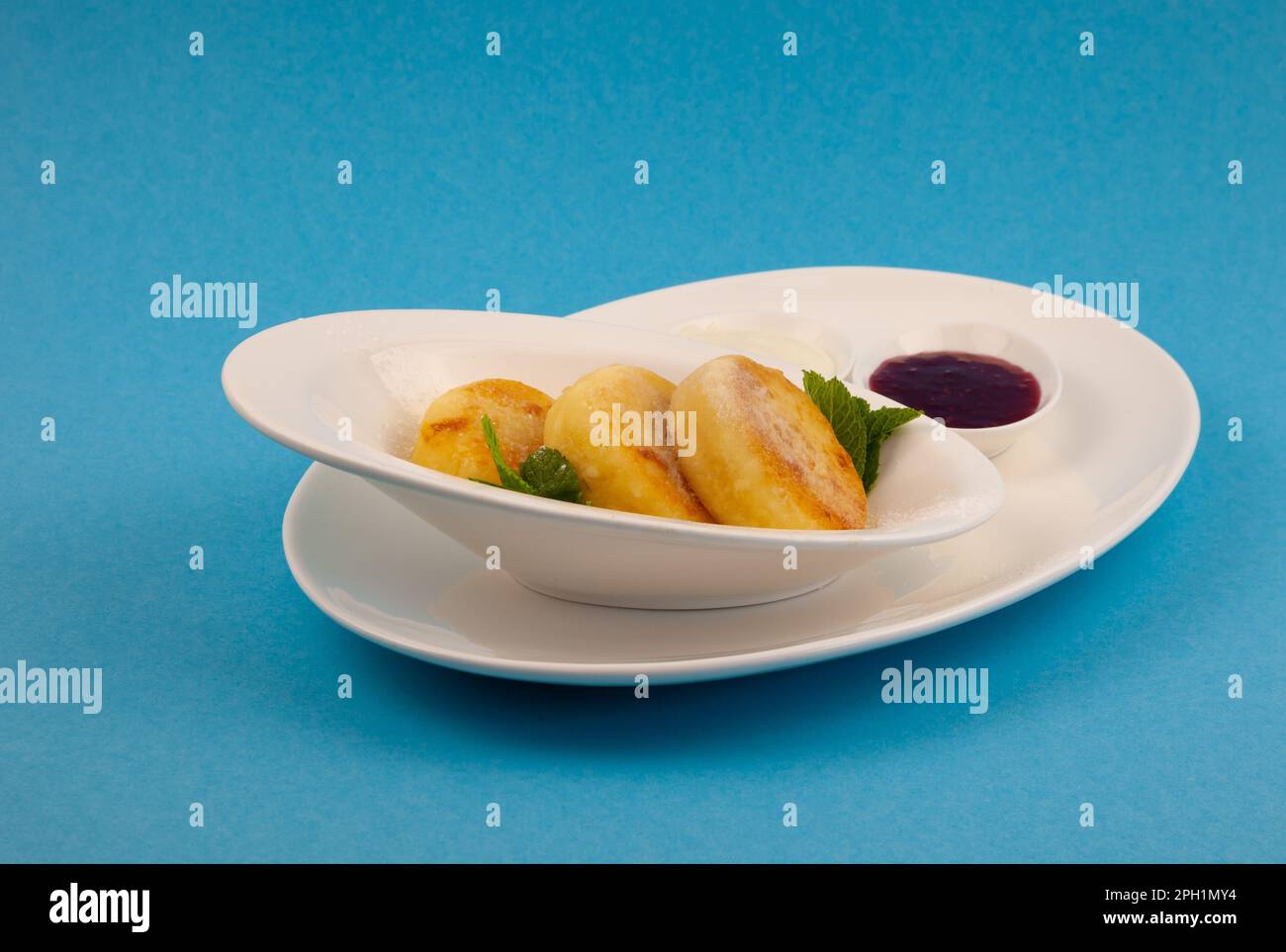 Frittelle di formaggio ricotta rotonda in un piatto bianco su sfondo blu. Cibo prima colazione. Cibo sano. Salsa di panna acida e menta. Primo piano vista dall'alto. Pasto dessert. Frittelle di ricotta al formaggio ricotta. Foto Stock