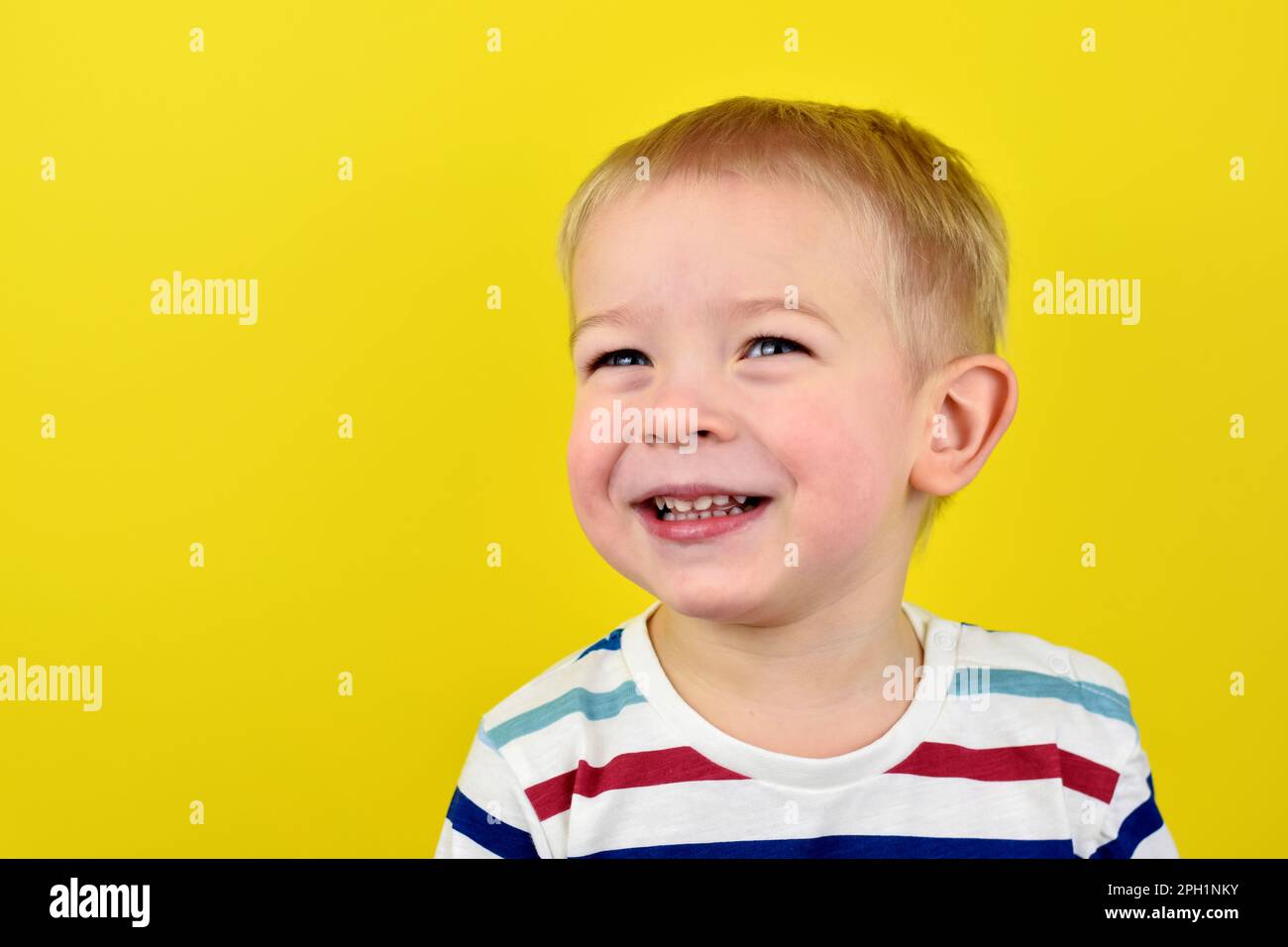 Primo piano Ritratto di un bel ragazzo ridendo. Adorabile bambino piccolo ride su sfondo giallo. Carino biondo ragazzo sorridendo e ridendo. Illuminat Foto Stock