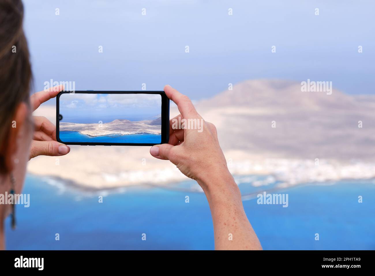 Una donna che fotografa l'isola la Graciosa con il suo smartphone. Lanzarote, Isole Canarie. Foto Stock