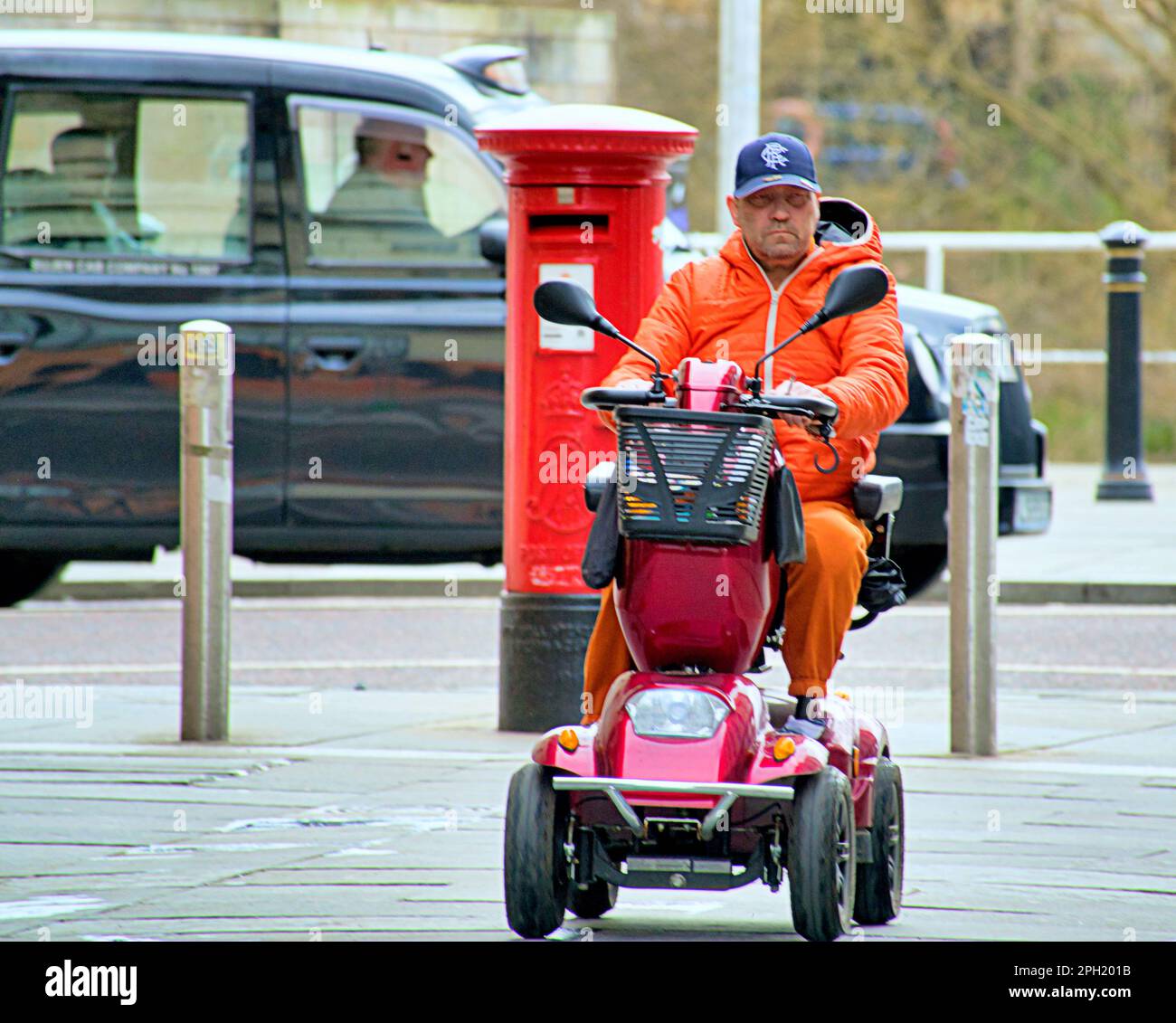 uomo con tuta a guscio arancione su uno scooter per la mobilità Foto Stock