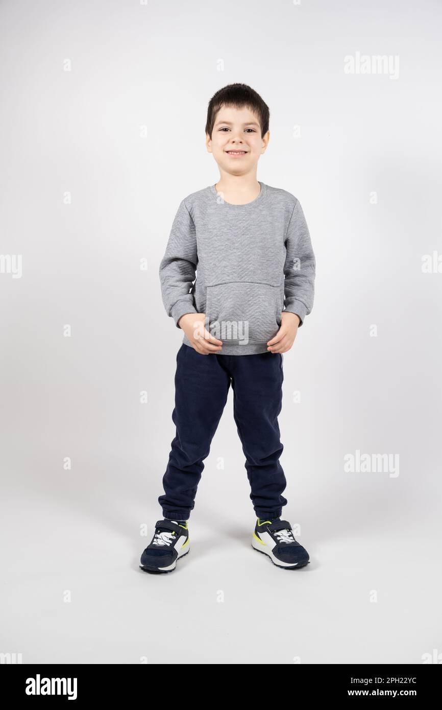 Un ragazzino in una felpa, pantaloni e sneakers su sfondo bianco. Abbigliamento e calzature per bambini Foto Stock