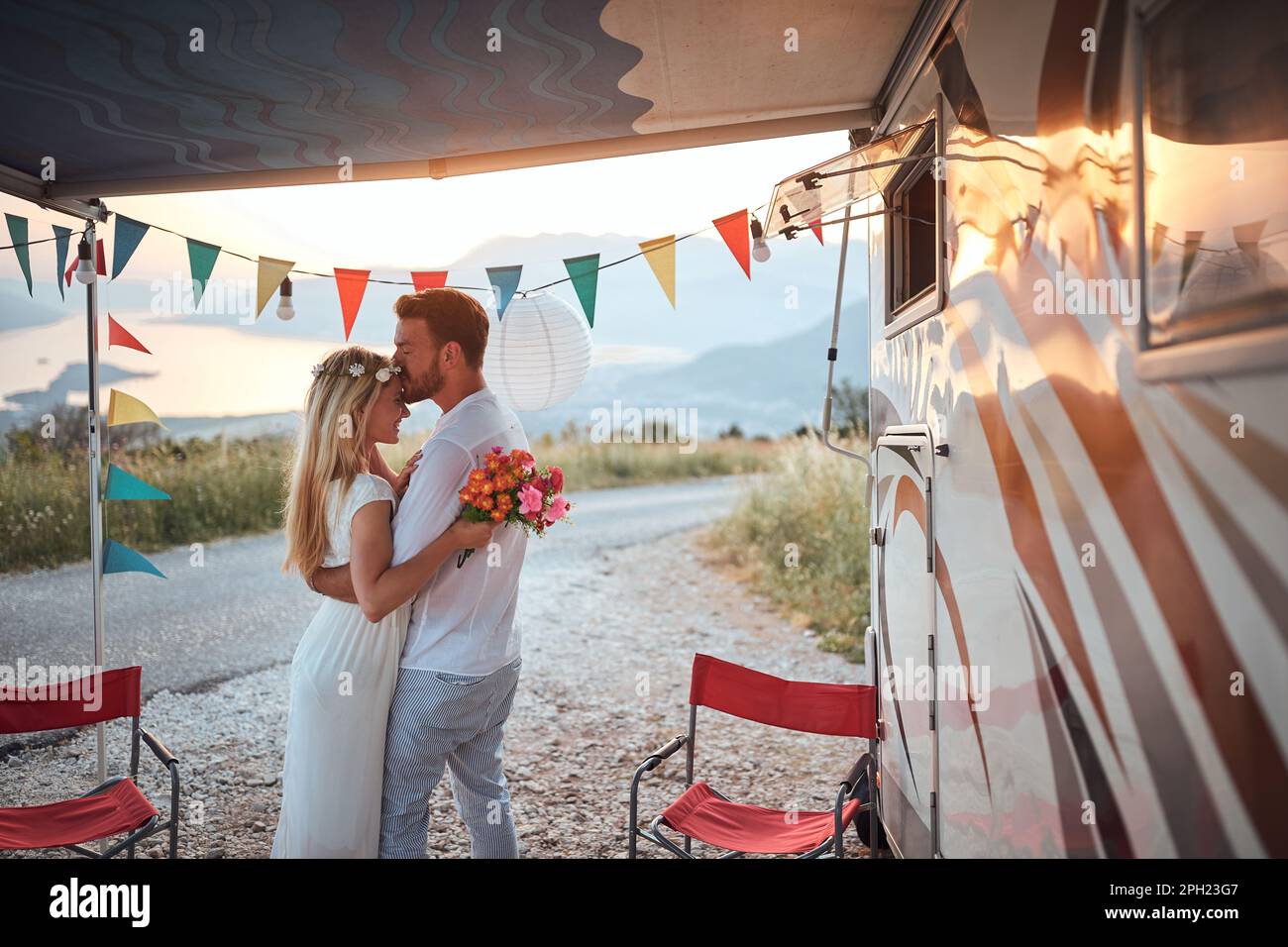 Sposi novelli di fronte al camper. L'uomo che dà un bacio alla fronte per sposare. Cerimonia nuziale, amore, concetto di natura Foto Stock