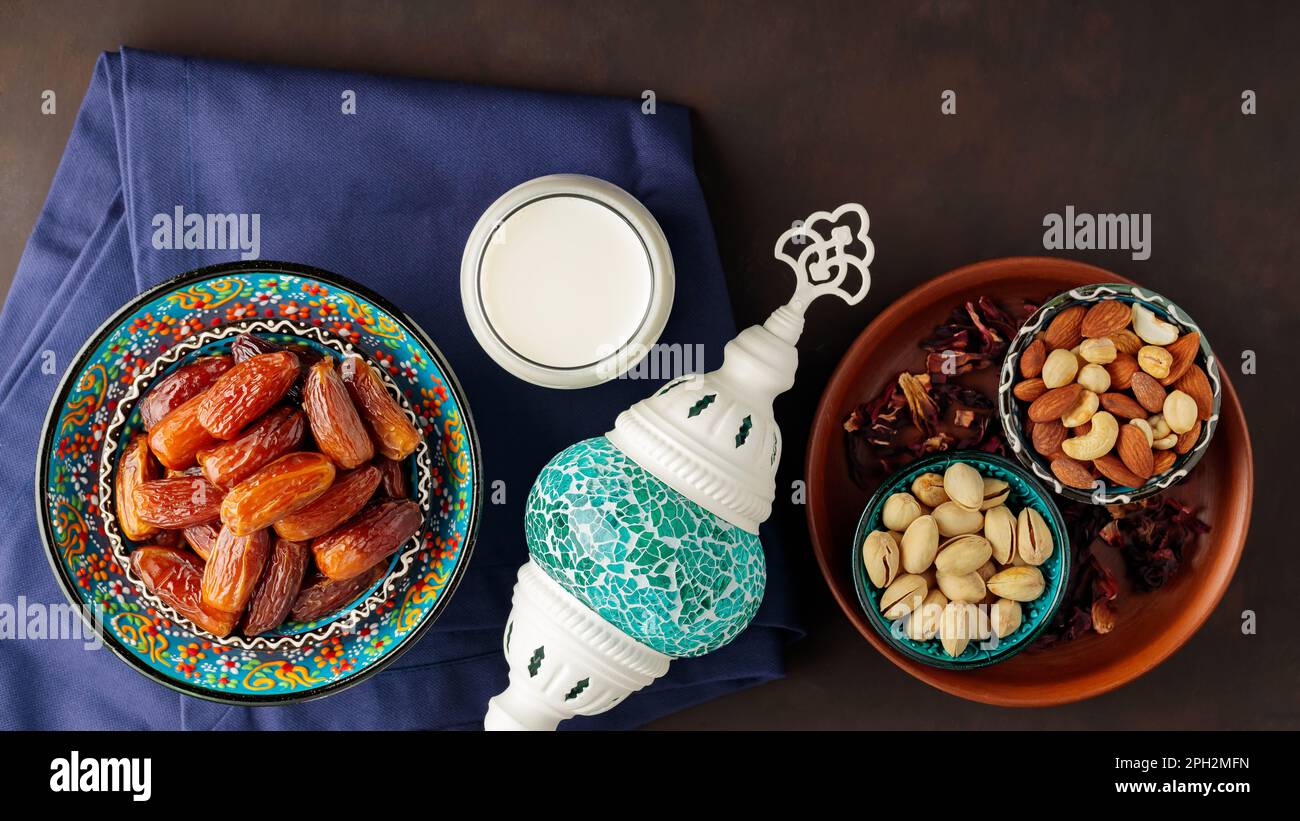 Datteri secchi, noci e latte su sfondo scuro. Ramadan Kareem e iftar cibo musulmano e lampada turca. Concetto Ramadan. Vista dall'alto Foto Stock
