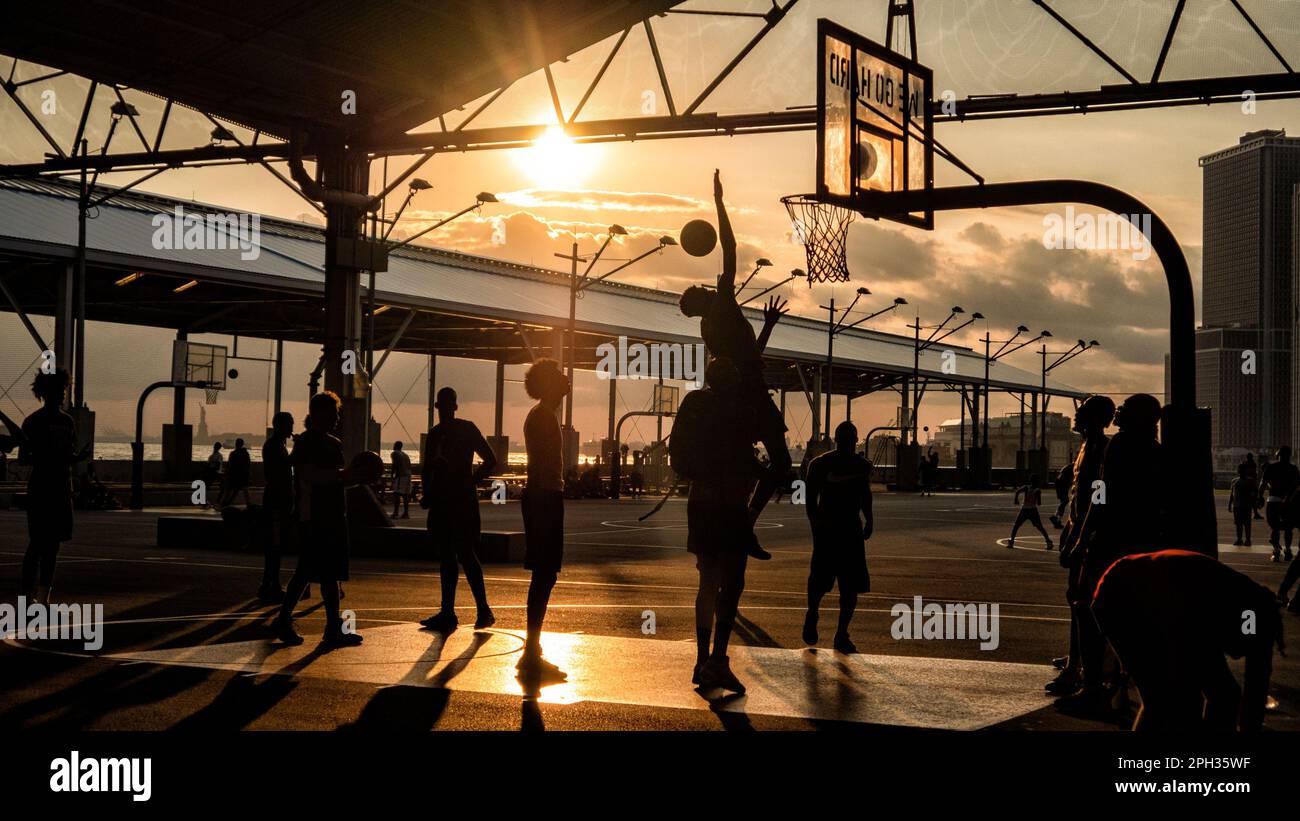 Persone che giocano a basket all'aperto al tramonto Foto Stock