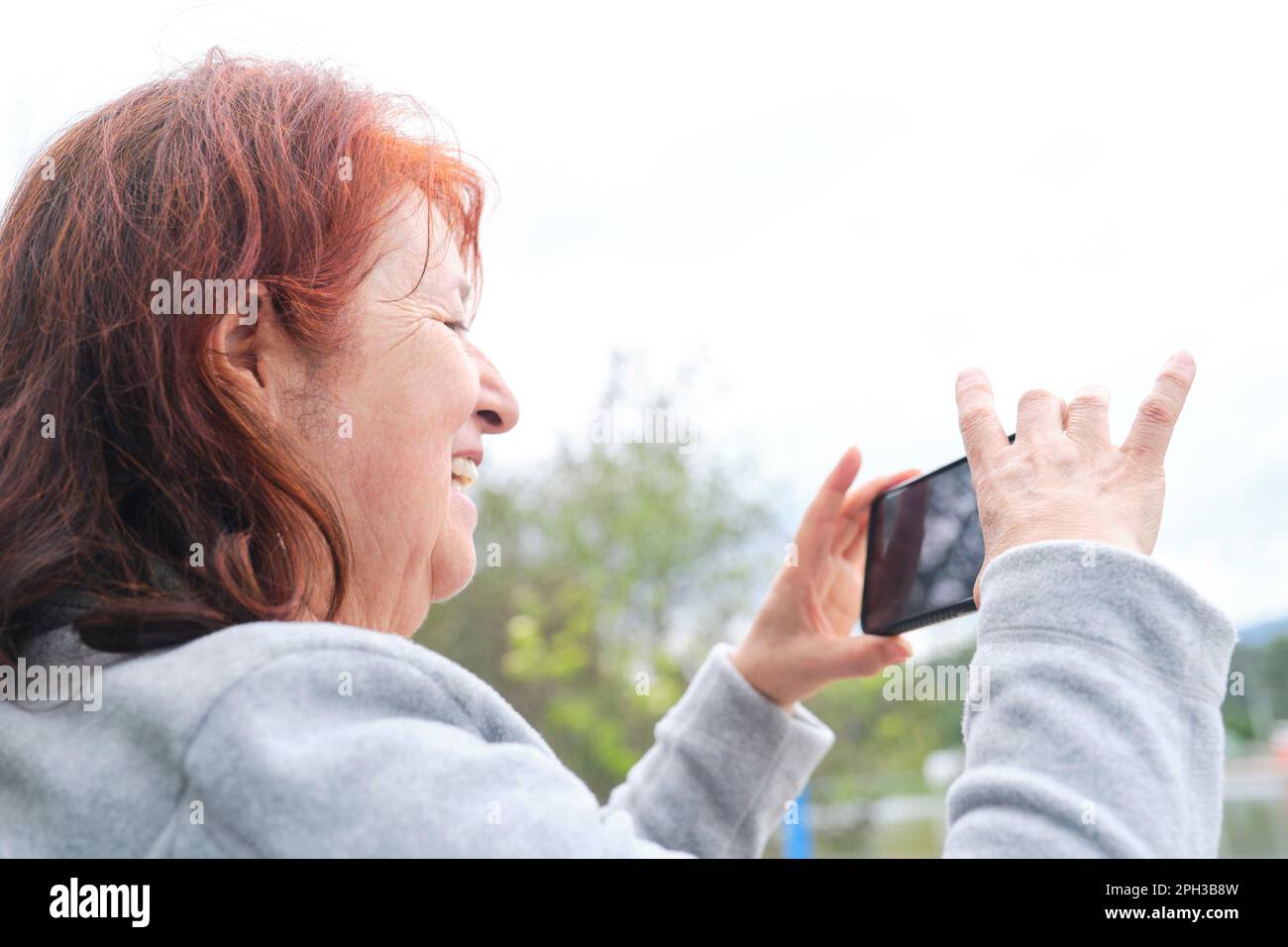 Donna matura latina sorridente mentre parla tramite videochiamata dal suo smartphone all'aperto. La tecnologia utilizzata per comunicare rende felici le persone. Foto Stock