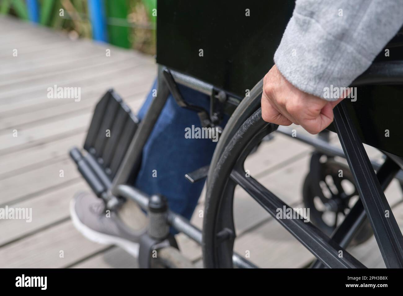 Donna irriconoscibile che passeggi in sedia a rotelle, all'aperto. Primo piano di una mano femmina che sposta la sedia a rotelle in avanti. Foto Stock