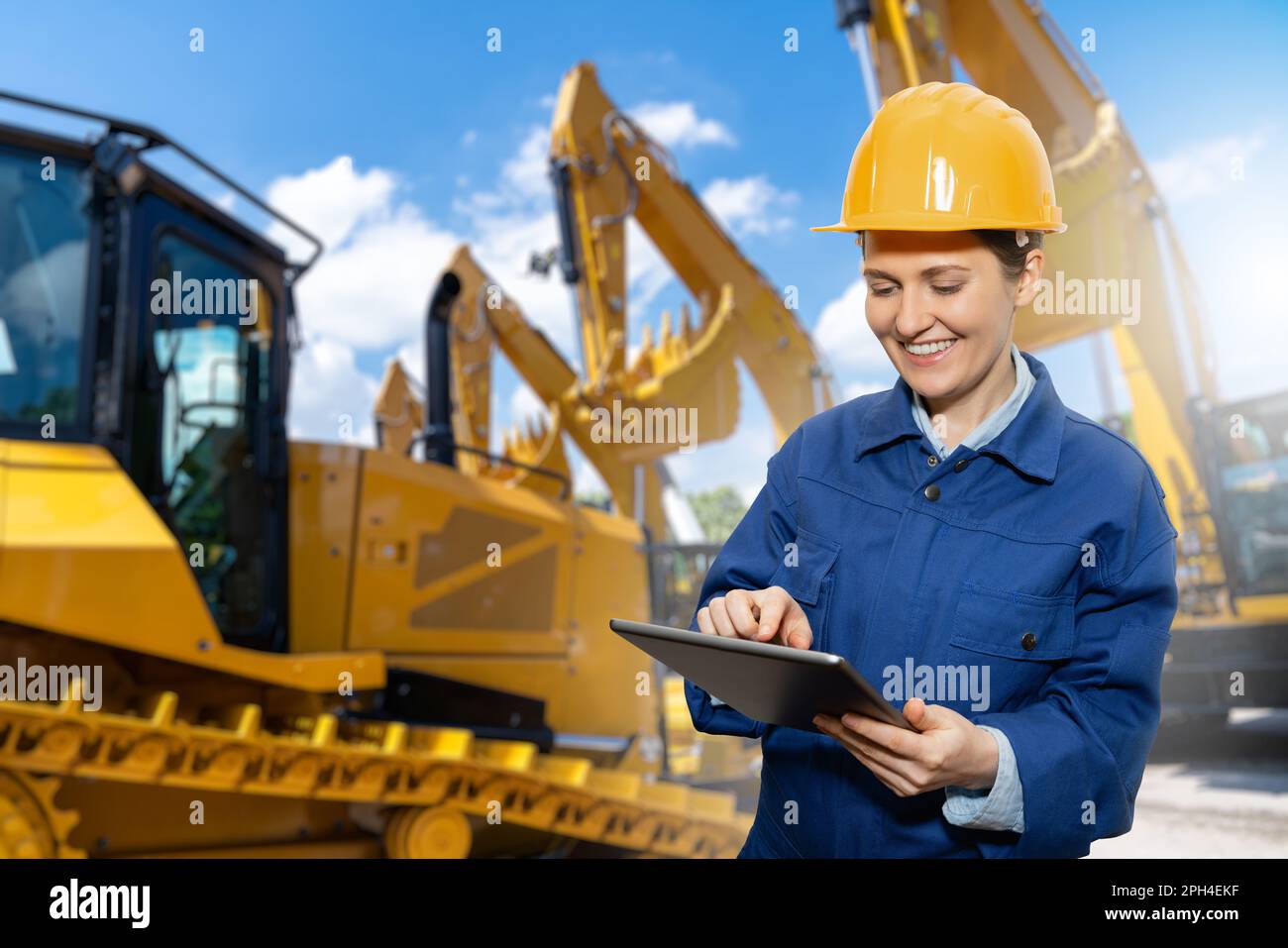 Ingegnere donna con casco e tablet digitale sullo sfondo delle macchine da costruzione. Foto di alta qualità Foto Stock