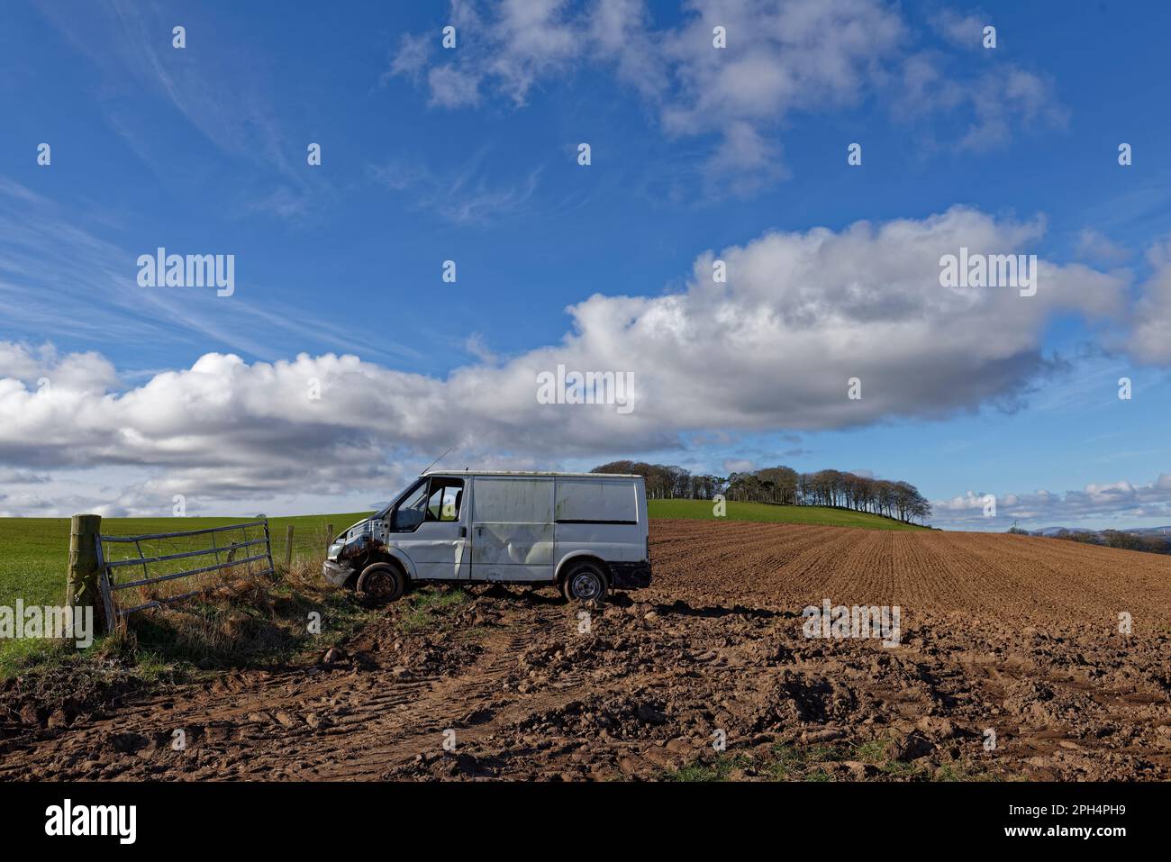 Un furgone bianco danneggiato e abbandonato parcheggiato in un campo arato vicino al bacino di Montrose, con un Ky blu e nuvole bianche sopra. Foto Stock