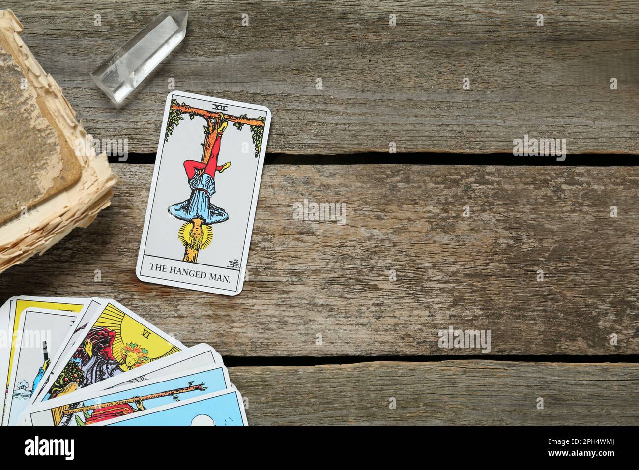 Impiccato uomo con altre carte tarocchi, cristallo e vecchio libro su tavola di legno, piatto. Spazio per il testo Foto Stock
