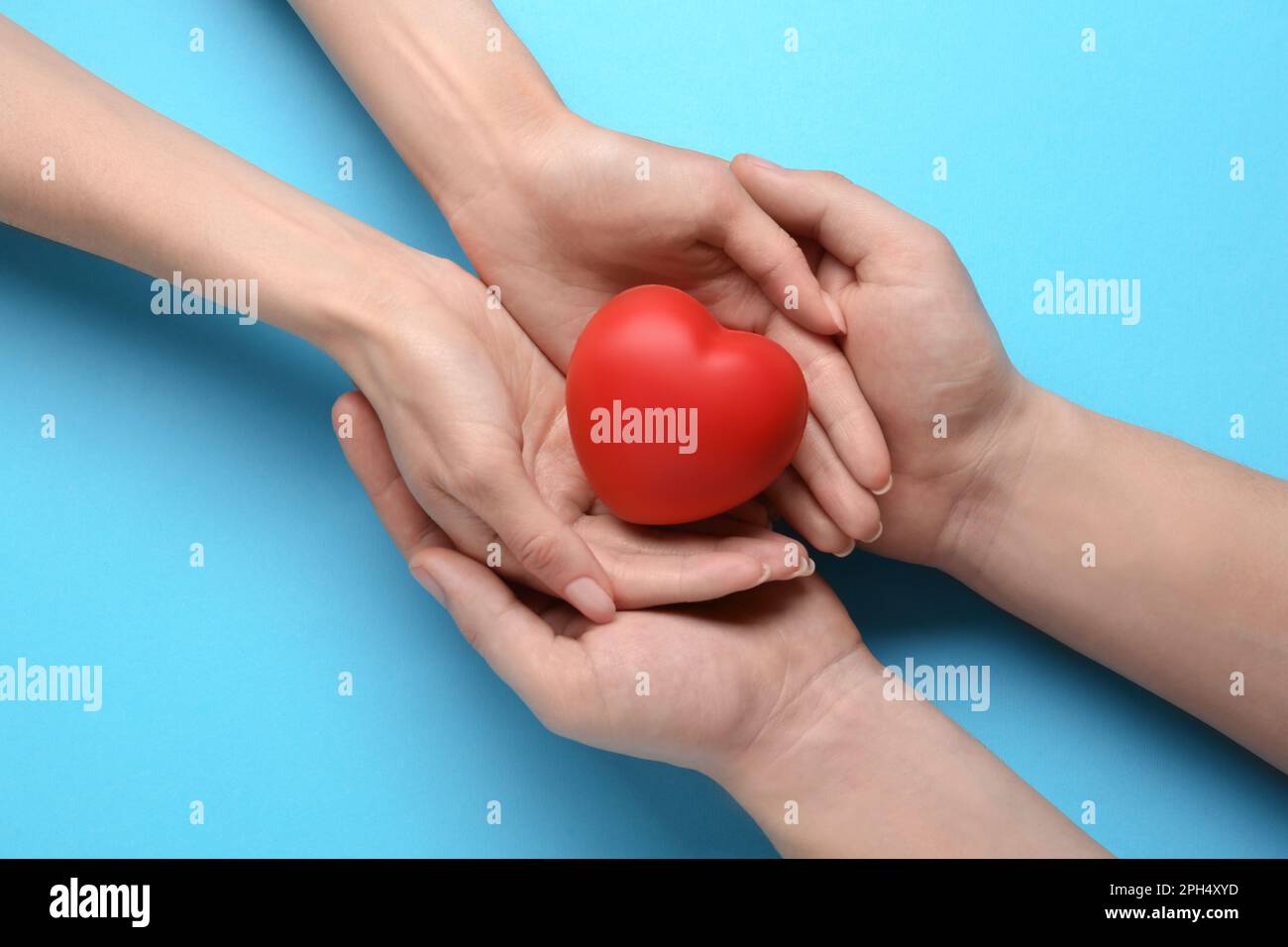 Persone che tengono rosso cuore decorativo su sfondo azzurro, vista dall'alto. Concetto di cardiologia Foto Stock