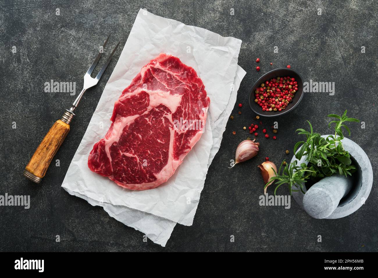 Bistecca di ribeye fresca cruda o bistecca di costolette. Carni fresche marmorizzate Ribeye Black Angus e condimenti pepe, rosmarino, timo e sale su legno vecchio rusti Foto Stock