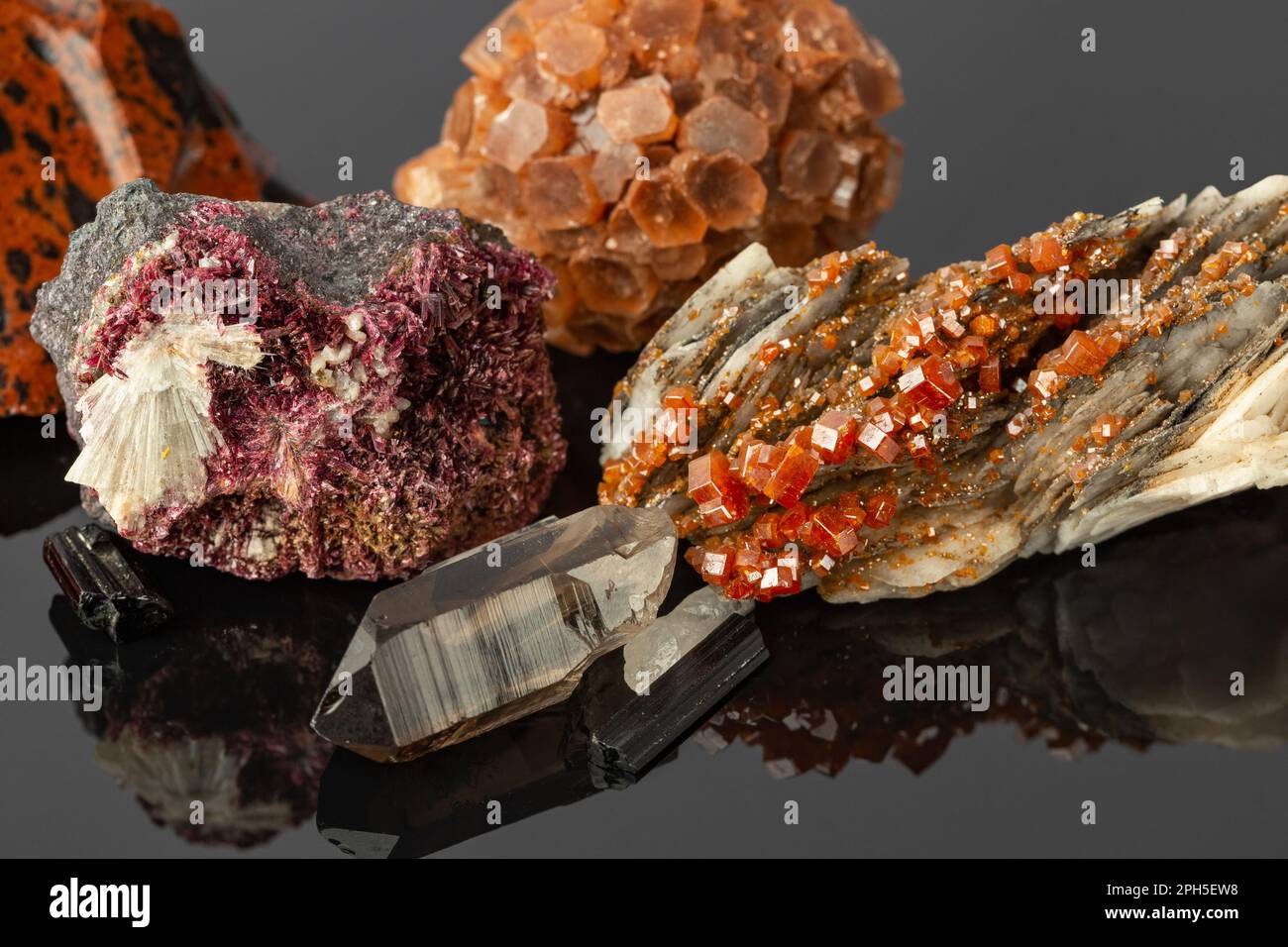 Foto ravvicinata del Gruppo delle pietre e dei minerali, tra cui Vanadinite su Barite, Aragonite Sputnik, cristalli di Erythrite su superficie riflettente Foto Stock