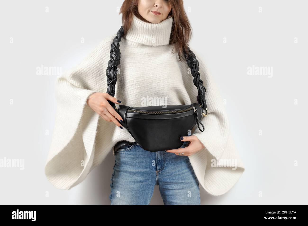 Donna che presenta il pacchetto Fanny in vera pelle nera con una bellissima tracolla intrecciata. Accessori in pelle fatti a mano Foto Stock