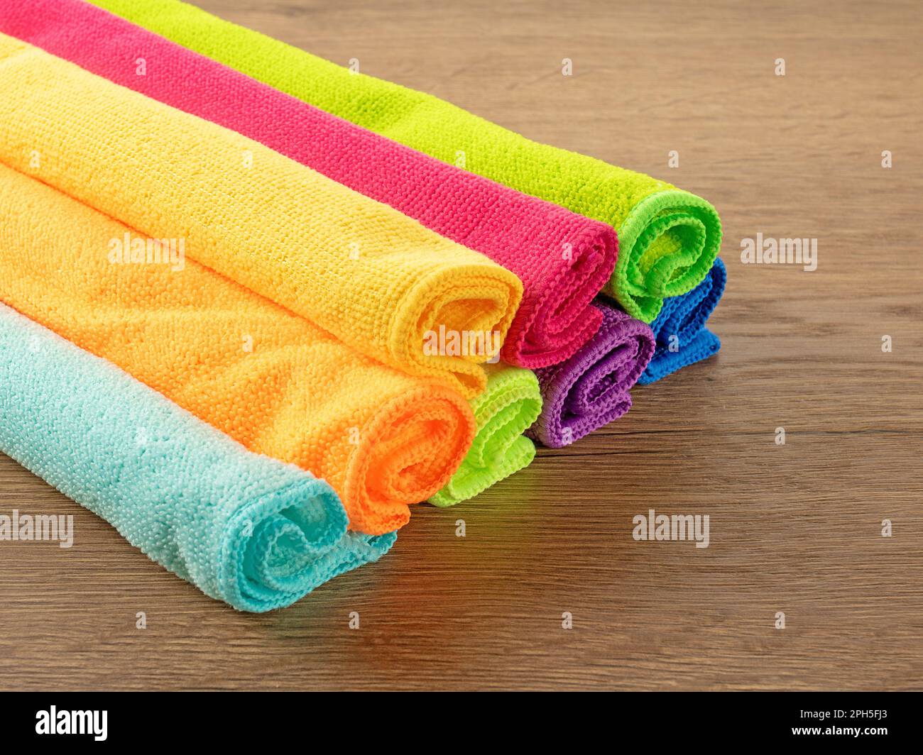 Pila di asciugamani in microfibra da cucina dai colori vivaci su un tavolo di legno marrone Foto Stock