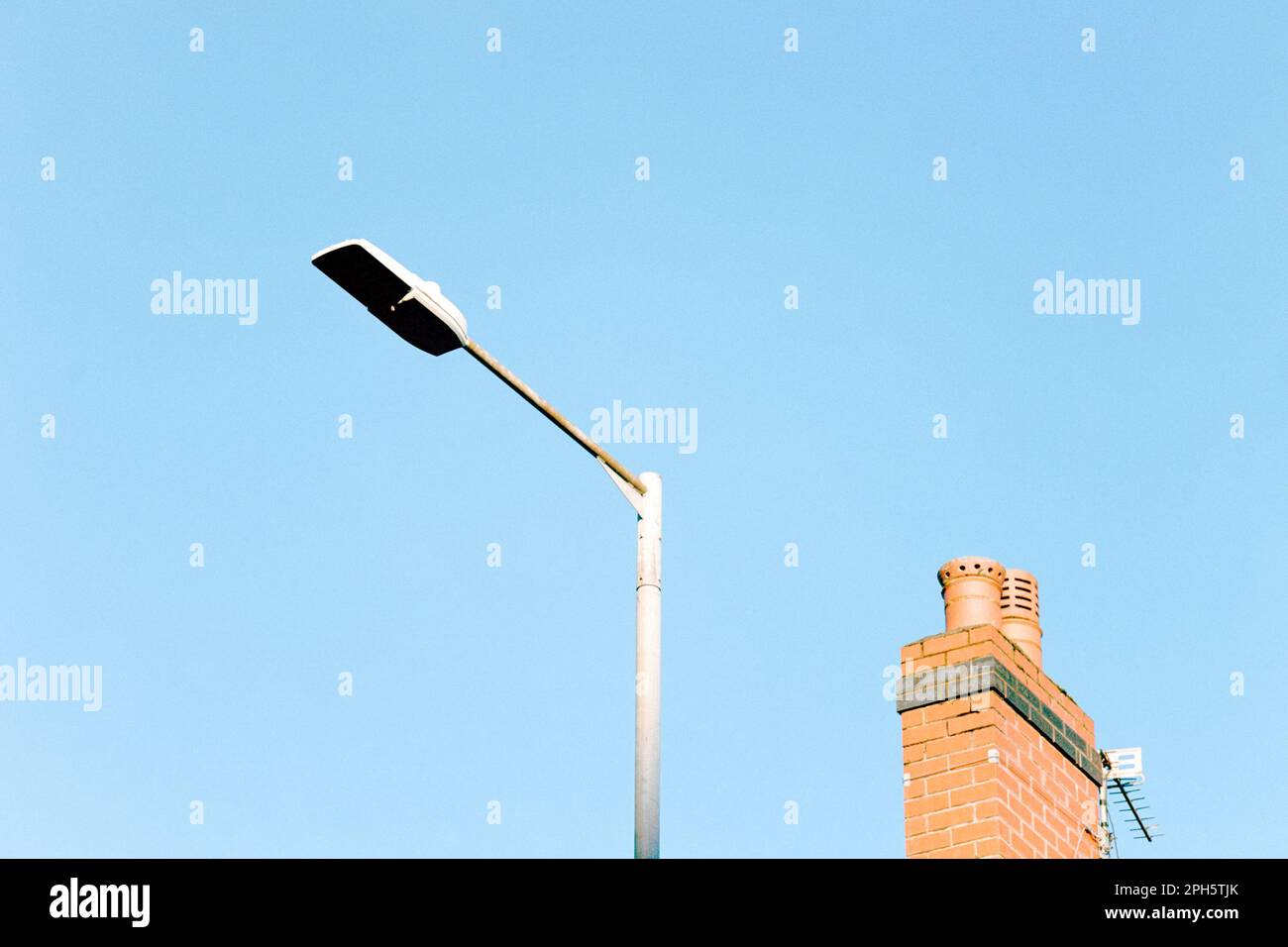 Foto minimalista di una lampada da strada e di un camino da un tetto vicino contro un cielo blu, Inghilterra, Regno Unito, con spazio copia Foto Stock
