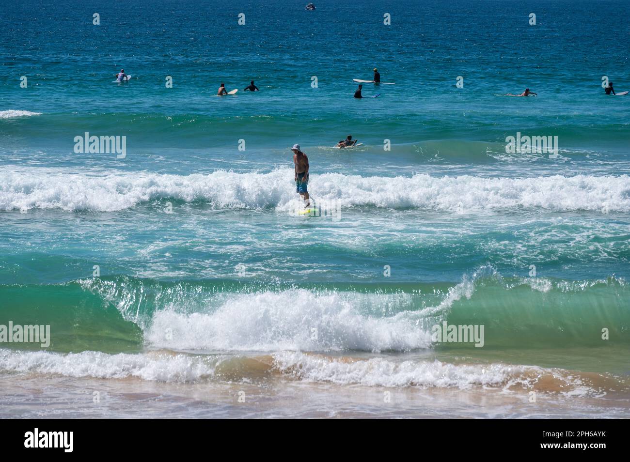 Le onde si rompono sulla spiaggia mentre un surfista cavalca le onde a Manly, Sydney, nuovo Galles del Sud, Australia sullo sfondo del blu Oceano Pacifico. Foto Stock