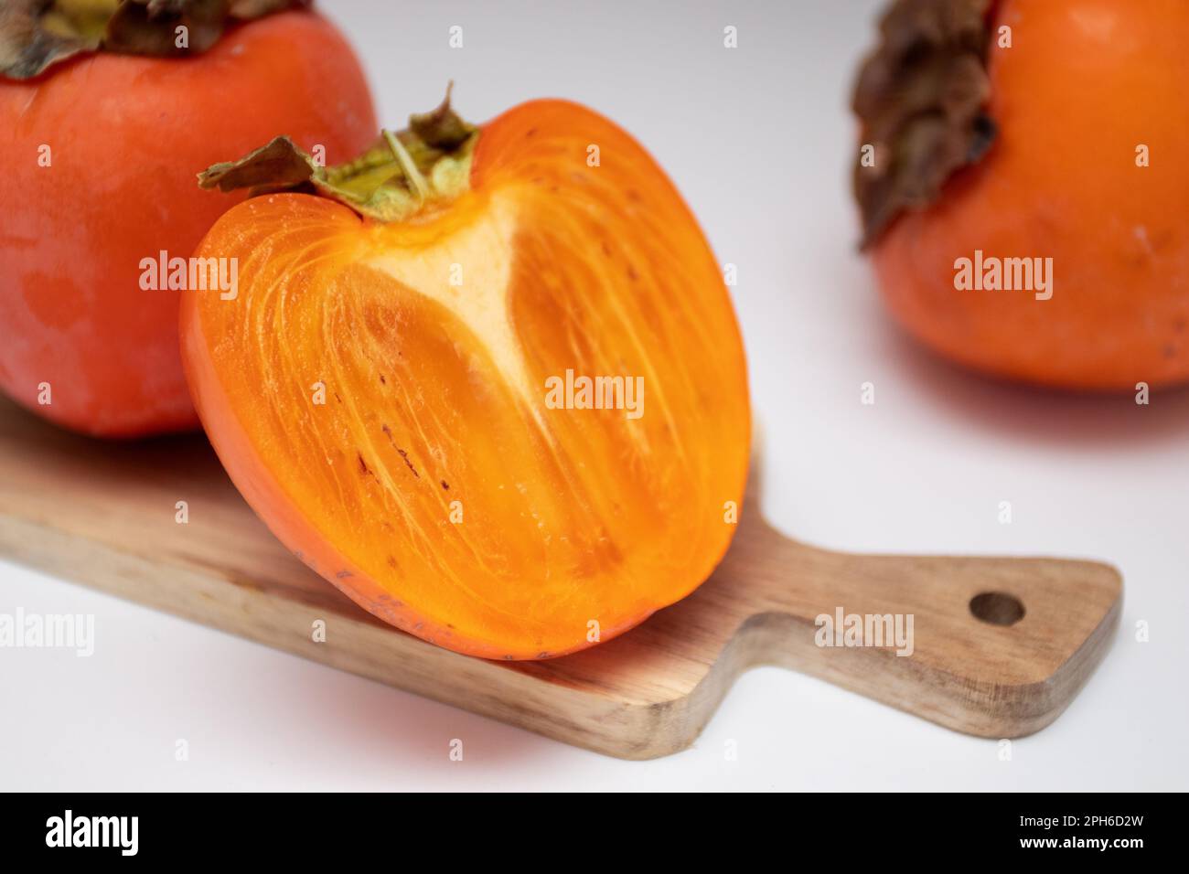 Persimmons freschi e metà di persimmons su asse di legno. Foto Stock