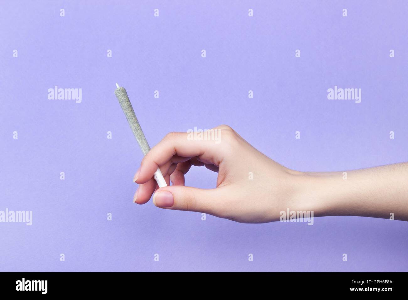 Una mano di donna con unghie naturali tiene un giunto con marijuana medica su uno sfondo viola chiaro. spazio di copia Foto Stock