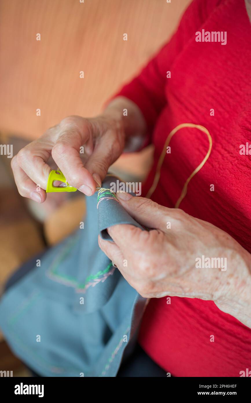 Donna anziana irriconoscibile che fa ricami con un ditale giallo. Interno Foto Stock