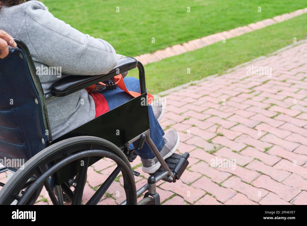 Donna irriconoscibile che passeggi su una sedia a rotelle spinta da qualcuno, su un sentiero, all'aperto. Foto Stock