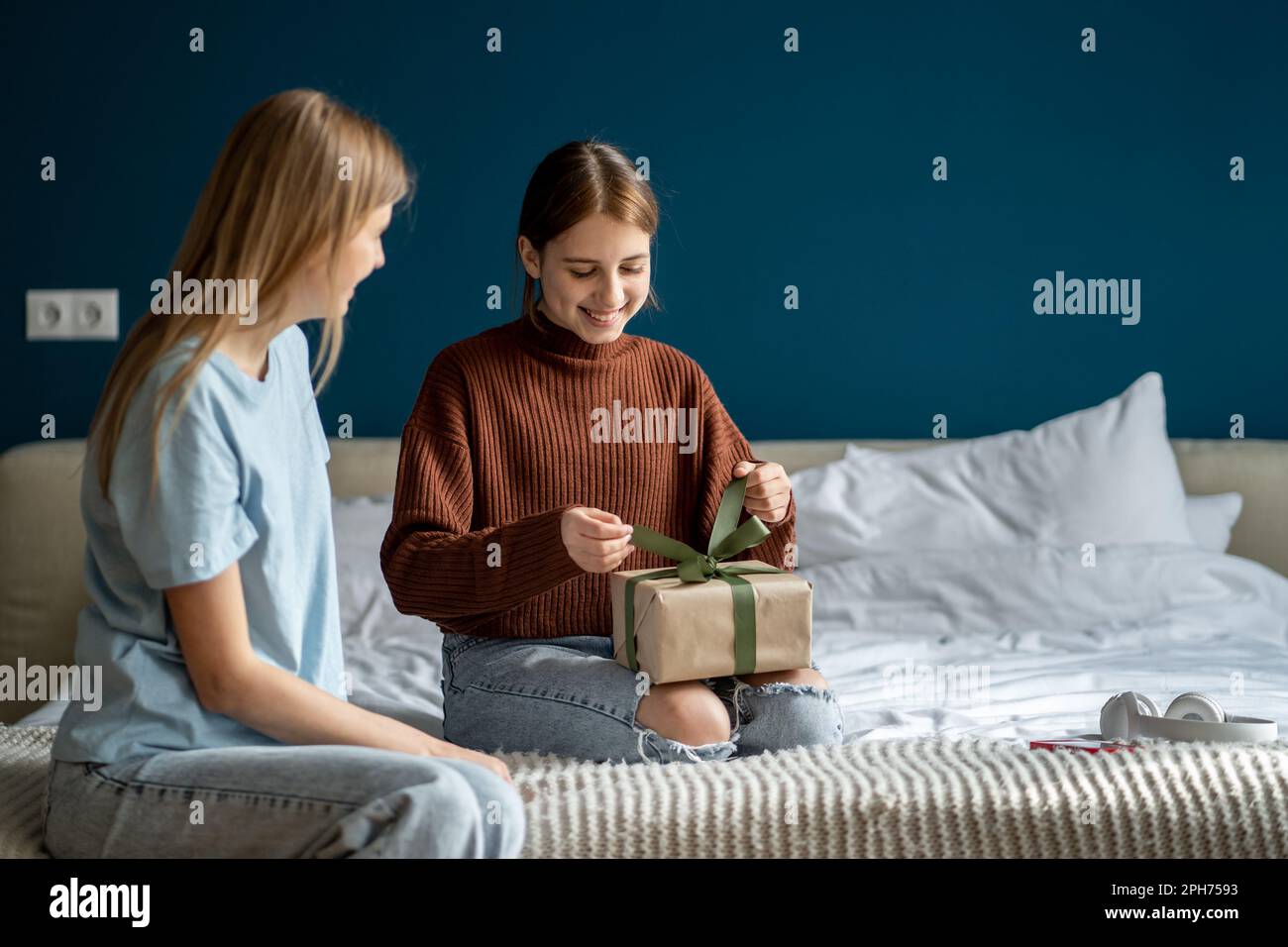 Donna gentile che cura la mamma che dà il regalo a felice figlia adolescente compiaciuta per il compleanno nella camera da letto domestica Foto Stock