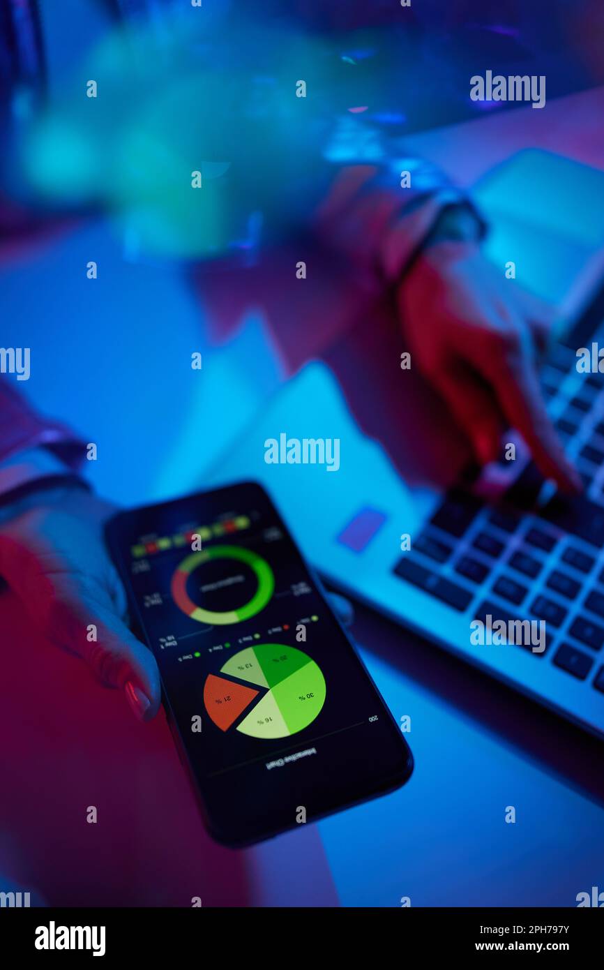 Concetto futuristico metaverso neon. Primo piano su una donna che utilizza un notebook, un'app per smartphone ed esplora le carte in ufficio. Foto Stock