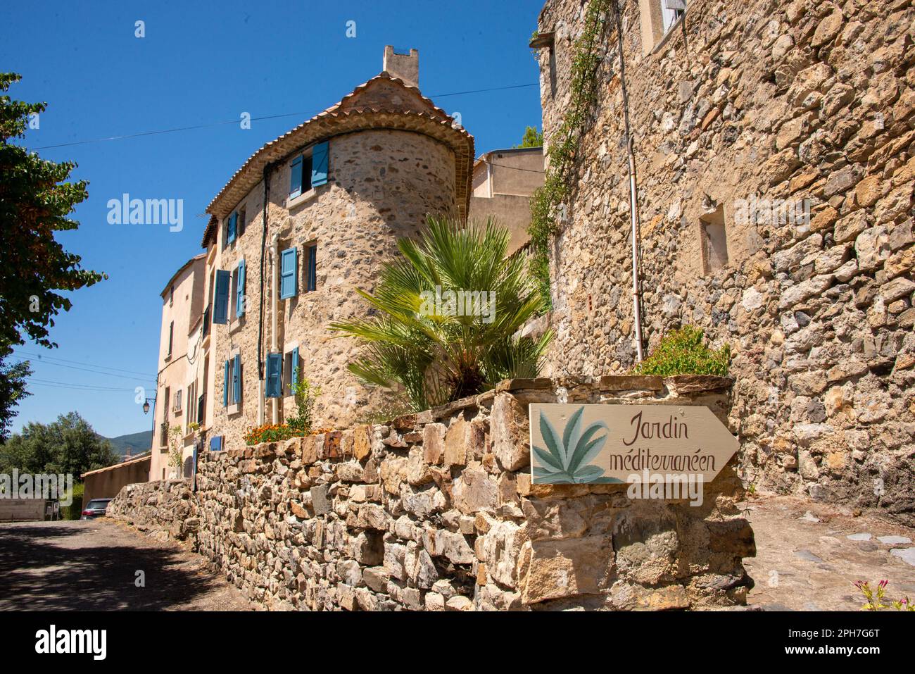 Un cartello conduce attraverso il pittoresco borgo medievale di Roquebrun al Giardino Mediterraneo passando per una casa particolare con un angolo tondo. Foto Stock