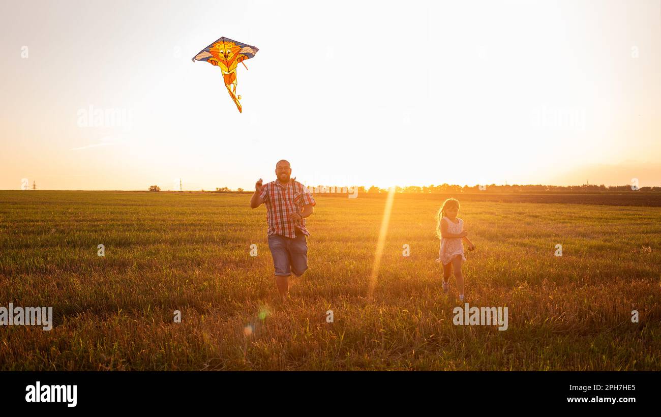 Il padre calvo in vetro corre intorno al campo con la figlia che mette nel aquilone del cielo. L'uomo millenario gioca con la ragazza nelle aree rurali. Viaggi, divertimento Foto Stock