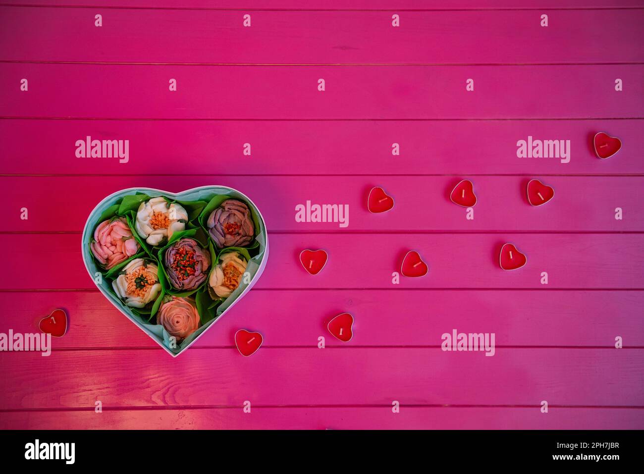 Su sfondo di legno rosa si trova una scatola di fiori di marshmallow commestibili, a forma di cuore con candele rosse. Vista dall'alto, fermo, piatto. Dolce regalo f Foto Stock