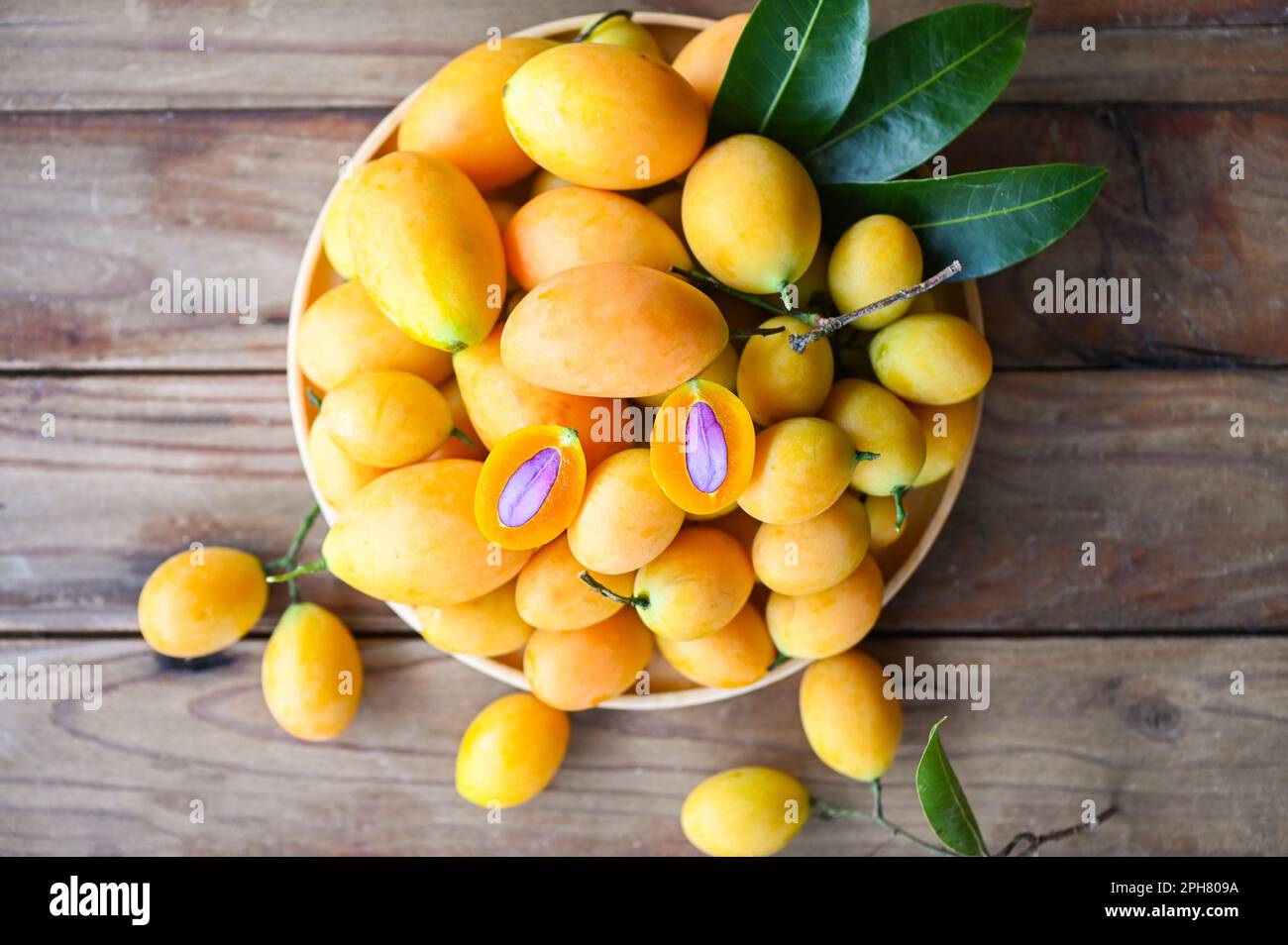 Frutti mariani di prugna e foglie in piatto su sfondo di legno, frutta tropicale Nome in Thailandia giallo dolce prugna mariana Maprang Plango o Mayong chid - t Foto Stock